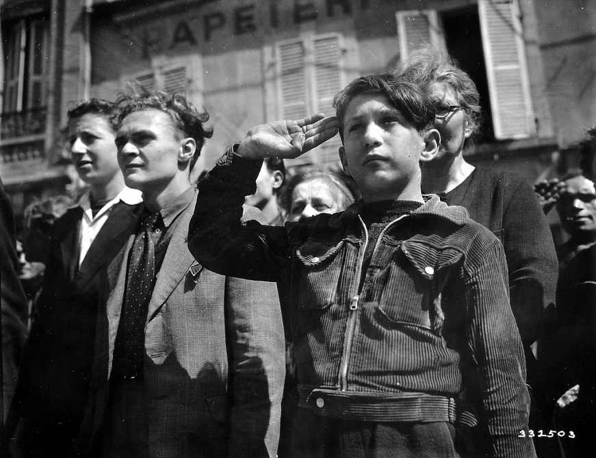 In a group of civilians, a young French boy is the salvation military during the national anthem at Cherbourg.jpg